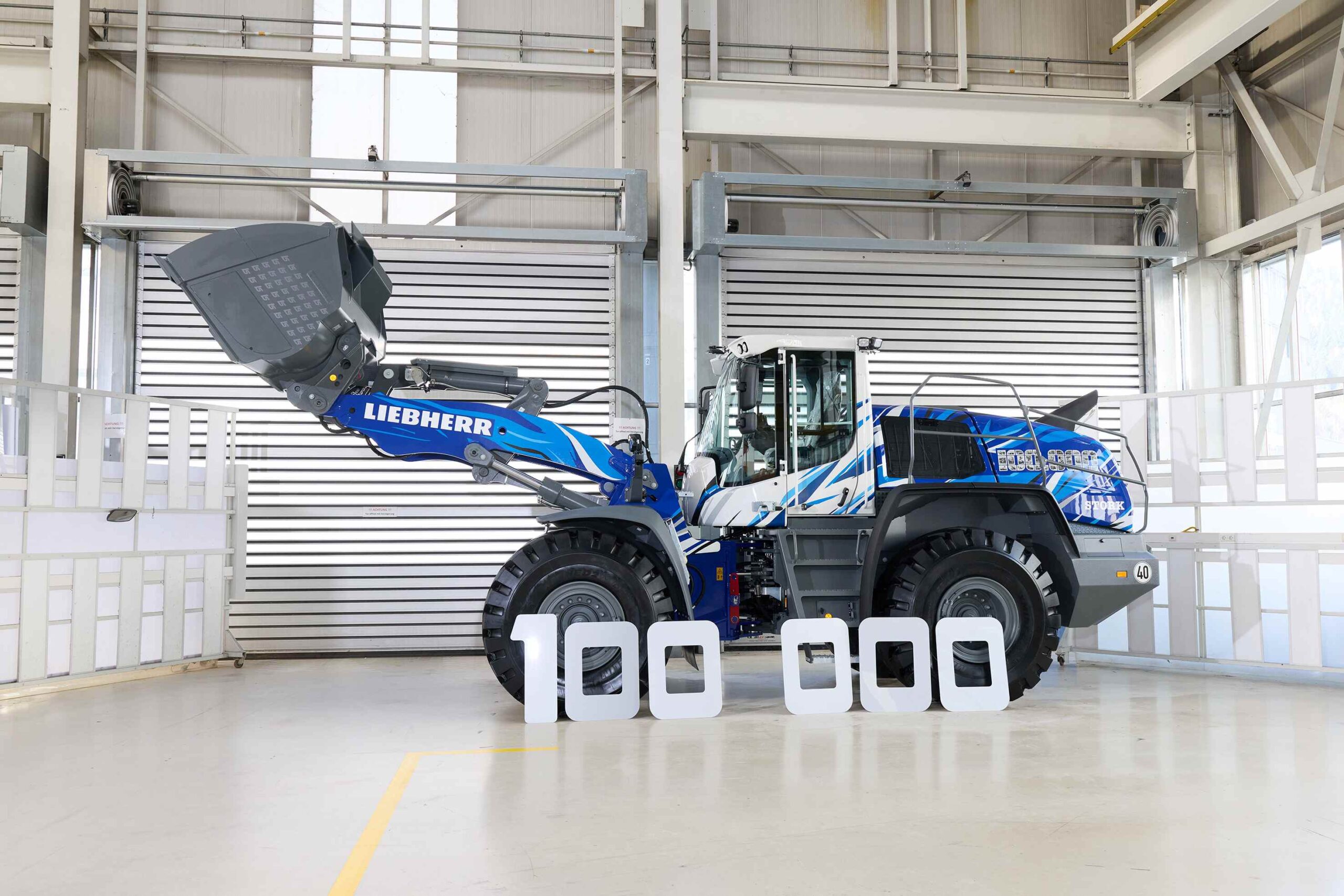 The ‘100 000’ lettering, composed of historical black-and-white images, traces the development of Liebherr wheel loaders.